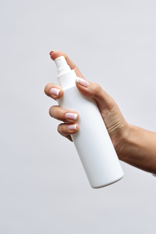 Person with manicured hands holding a white spray bottle
