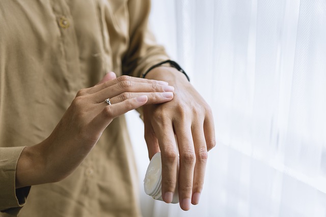Person in a tan shirt wearing a diamond ring applying lotion to their hand