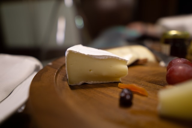 A slice of brie on a brown board along with other fruits and cheeses