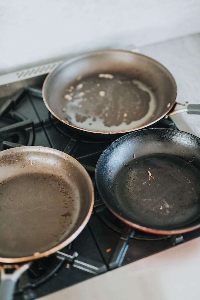 Three dirty pans on a stovetop filled with grease and potential food for roaches, one of the factors that can extend the lifespan of a roach