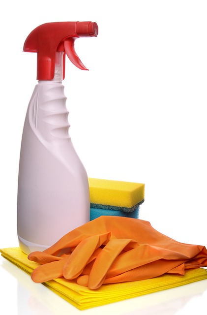 Pink and red spray bottle beside yellow sponges and orange gloves