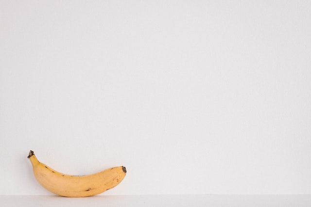 Lone yellow banana with brown spots against a white background