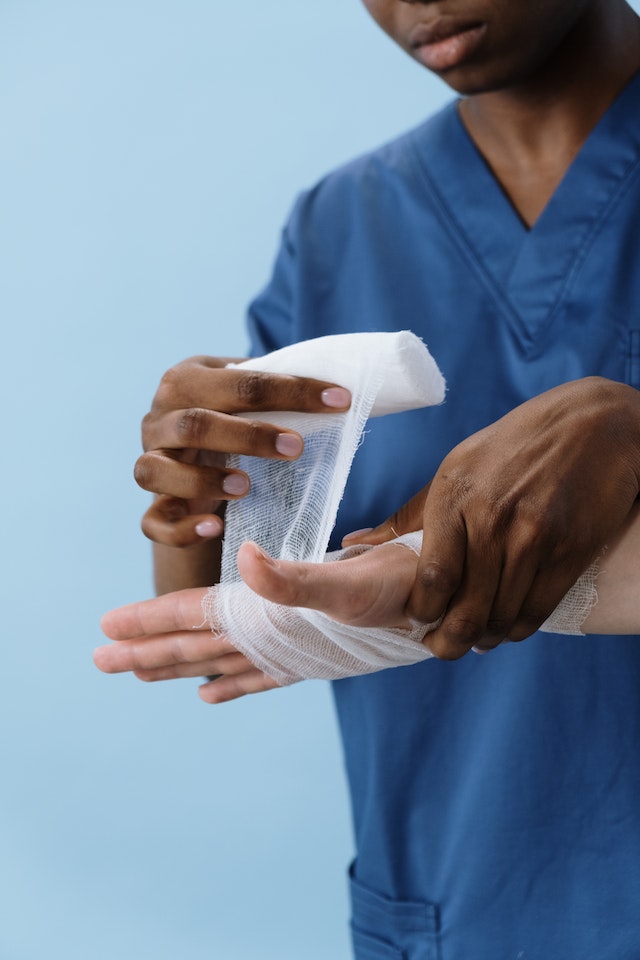 A person in blue scrubs bandaging someone's hand