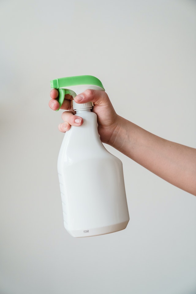 Person holding a white spray bottle with a green top