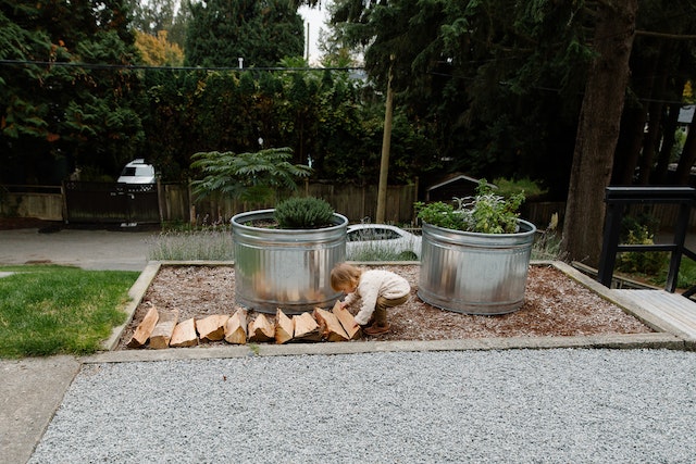 young child pushing wood around a garden with tin planters.