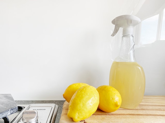 A spray bottle filled with lemon juice alongside three lemons
